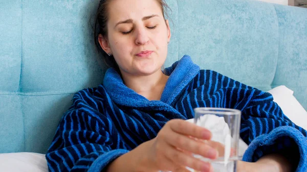 Porträt einer kranken jungen Frau, die unter Schmerzen leidet und ein Glas Wasser in der Hand hält — Stockfoto