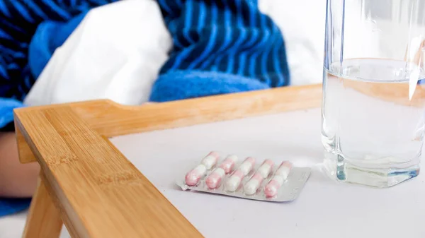 Closeup image of pills in blister and glass of water on tray in bed — Stock Photo, Image