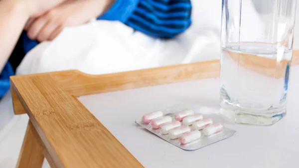 Closeup image of pills packed in blister lying on wooden tray next to bed — Stock Photo, Image