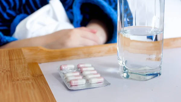 Close-up beeld van verpakte pillen en glas helder water op houten dienblad in bed — Stockfoto