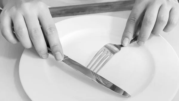 Czarno-białe zdjęcie zbliżenie kobieta trzyma widelec i nóż ciągu pustego naczynia na stół — Zdjęcie stockowe