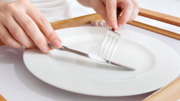 Foto de cerca de manos femeninas sosteniendo tenedor y cuchillo sobre un plato vacío. Concepto de dieta y adelgazamiento — Foto de Stock
