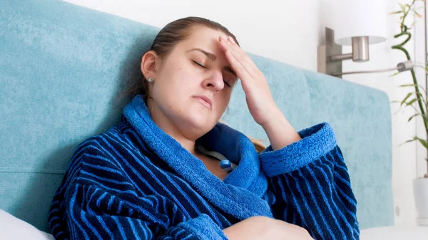 Portrait of young sick woman suffering from fever and head ache lying in bed — Stock Photo, Image