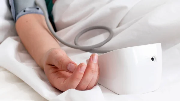 Foto de primer plano de la mano femenina y monitor digital de presión arterial en la cama —  Fotos de Stock