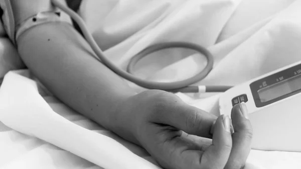 Immagine in primo piano in bianco e nero della mano femminile che misura la pressione sanguigna con manometro digitale — Foto Stock