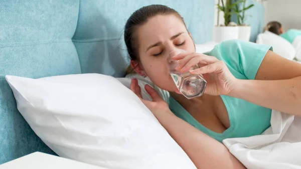 Портрет молодої жінки, що лежить у ліжку питна вода зі скла — стокове фото