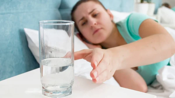Potret wanita sakit mengambil segelas air dari meja samping tempat tidur — Stok Foto