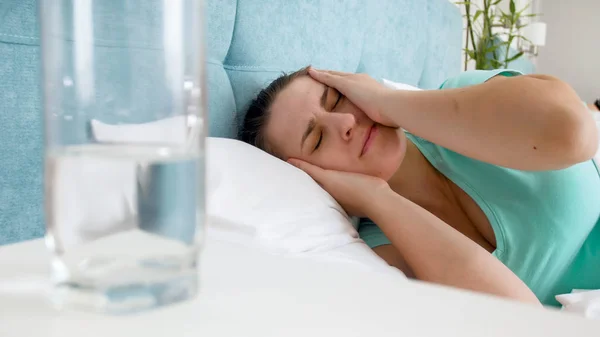 Närbild porträtt av sjuk kvinna med huvudvärk efter baksmälla i sängen — Stockfoto