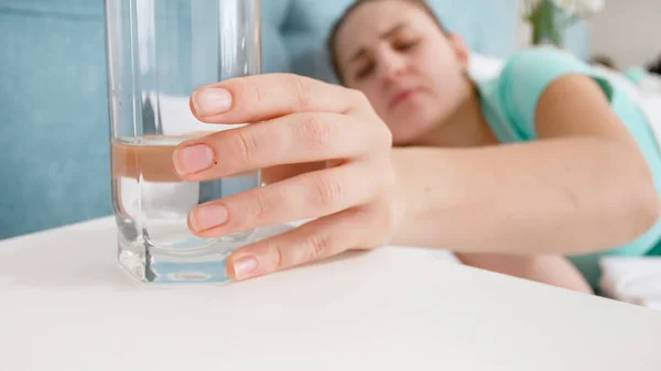 Foto di primo piano di una donna malata che prende un bicchiere d'acqua dal comodino — Foto Stock