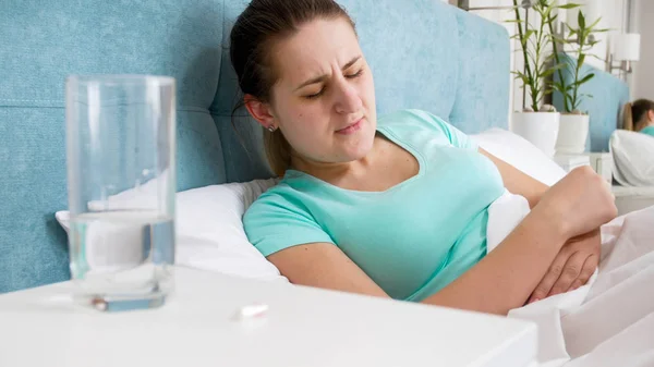Portrait of young woman with periods suffering from stomach ache lying in bed — Stock Photo, Image