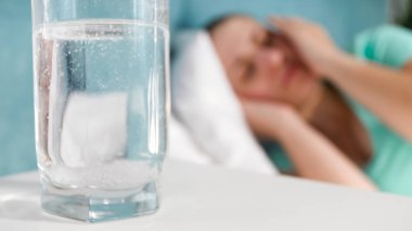 Bardak su çözünmüş aspirin baş ağrısı acı ve yatakta yatan kadın karşı