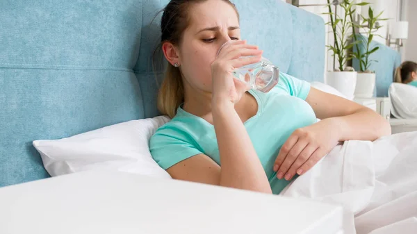Portrait of woman feeling unwell lying in bed and drinking water — Stok Foto