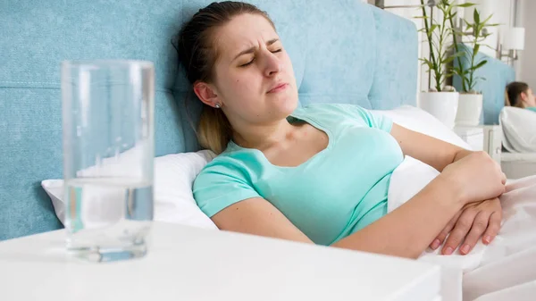 Retrato de una mujer joven acostada en la cama y sufriendo de dolor de estómago —  Fotos de Stock