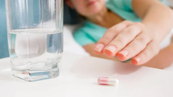 Closeup image of female hand reaching for pill lying on bedside table — Stock Photo, Image