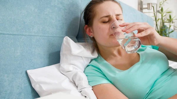 Potret wanita muda sakit berbaring di tempat tidur dan minum air dari kaca — Stok Foto