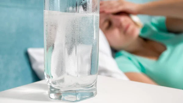 Immagine primo piano di vetro di acqua gassata sul comodino accanto alla donna malata sdraiata a letto — Foto Stock