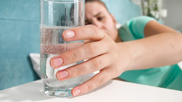 Closeup image of young woman taking glass of water with dissolved aspirin from bedside table — Stock Photo, Image