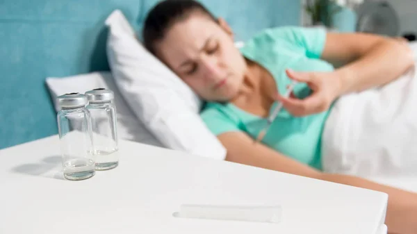 Out of focus image of sick woman lying in bed and making herself injection with syringe — Stock Photo, Image