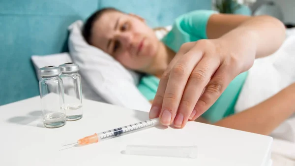 Крупним планом фото молодої жінки, яка страждає від болю в ліжку і приймає шприц, щоб зробити собі ін'єкцію знеболюючих препаратів — стокове фото