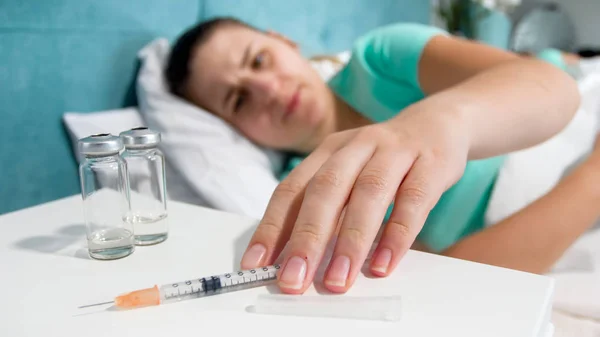 ベッドとベッドサイドのテーブルから取って注射器で薬物中毒を持つ若い女性のクローズ アップ画像 — ストック写真