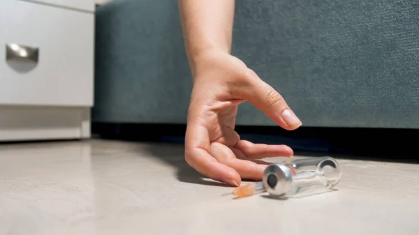 Imagen de primer plano de la mano femenina acostada en el suelo junto a la jeringa vacía y la ampolla. Concepto de sobredosis y adición de drogas —  Fotos de Stock