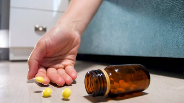 Close-up foto van fles pillen uit vrouwelijke hand liggend op de vloer vallen. Drugsverslaving. Overdosis drugs of medicijnen. Dood van de patiënt — Stockfoto