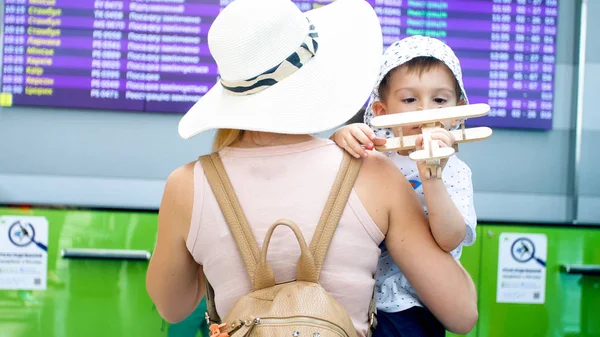 Ung mor omfamnar hennes småbarn son leker med leksak flygplan i flygplats — Stockfoto
