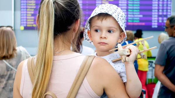 Retrato de uma jovem mulher abraçando seu filho na tela grande com horário de partida do voo no aeroporto — Fotografia de Stock