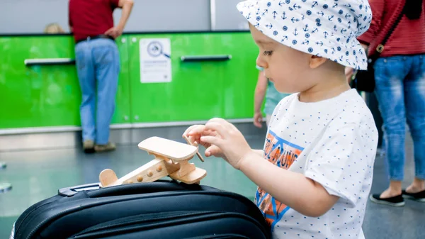 Крупный план маленького мальчика, играющего с игрушечным самолетом на большом чемодане в аэропорту — стоковое фото