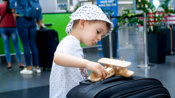 Портрет маленького мальчика, играющего с миниатюрным деревянным самолетом в терминале аэропорта — стоковое фото