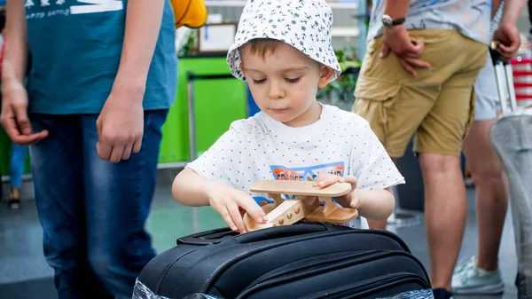 Retrato del niño pequeño esperando el primer vuelo en la terminal del aeropuerto y jugando con el avión de juguete — Foto de Stock
