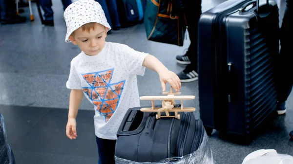 Liten toddler pojke står i kön för incheckning och leker med leksak trä flygplan. Barn reser. Unga turist. — Stockfoto