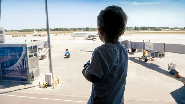 Silhuetten av liten toddler pojke tittar på flygplan genom stora fönster i flygplats — Stockfoto