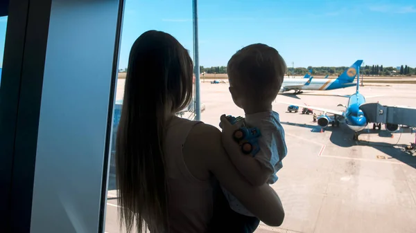 Silhueta de jovem mãe segurando seu filho em uma grande janela no terminal do aeroporto — Fotografia de Stock