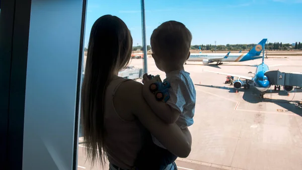 Silueta mladá žena s dítětem na letadla oknem na letišti — Stock fotografie