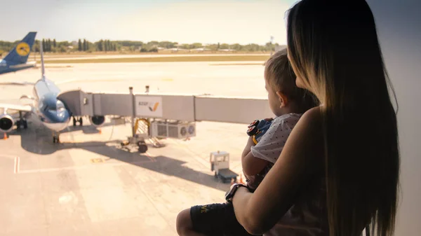 Retrato tonificado de jovem mãe com criança olhando em aviões no terminal do aeroporto — Fotografia de Stock