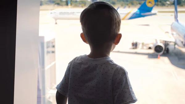 Silueta de niño pequeño mirando en el avión de aterrizaje en el aeropuerto internacional — Foto de Stock