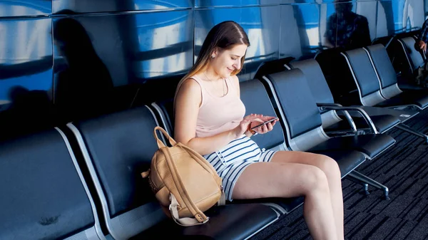 Portrait of beautiful smiling woman using smartphone while waiting for flight in airport — Stock Photo, Image