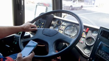 Closeup photo of truck driver typing on smartphone while driving. Danger in transport. Irresponsible driver clipart