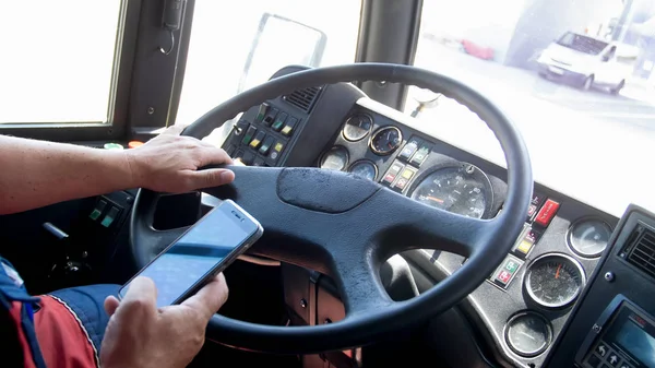 Крупный план водителя, держащего смартфон во время вождения автобуса — стоковое фото