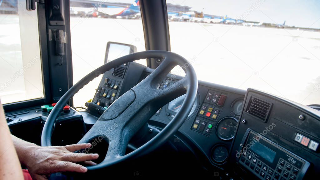 Closeup image of driver hands on steering wheel of bus driving on airport runway