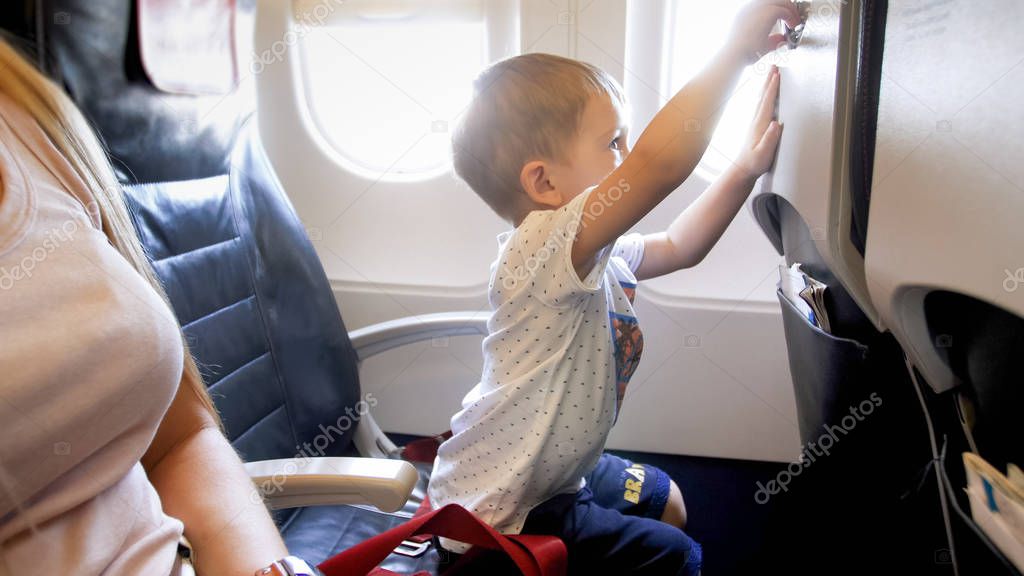 Little 2 years old boy playing with foldable table in airplane