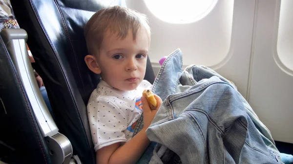 Retrato del niño pequeño sentado en el avión y comiendo croissant — Foto de Stock