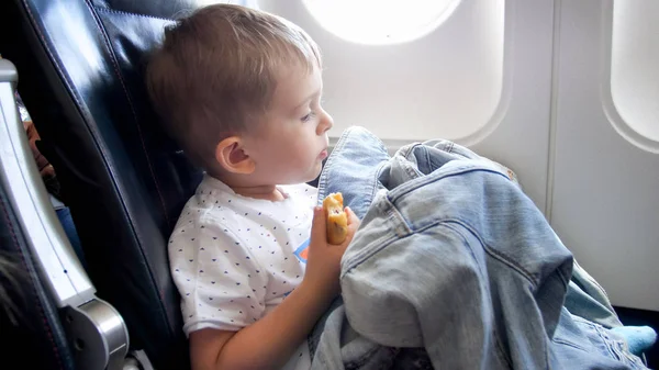 Porträt eines süßen Kleinkindes, das im Flugzeug sitzt und Brötchen isst — Stockfoto