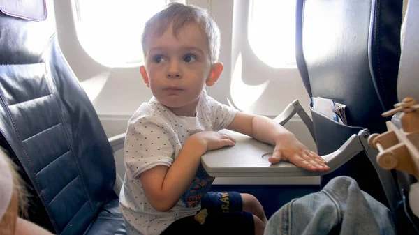 Pequeño niño sentado junto a la ventana en el avión y lloking en la madre — Foto de Stock