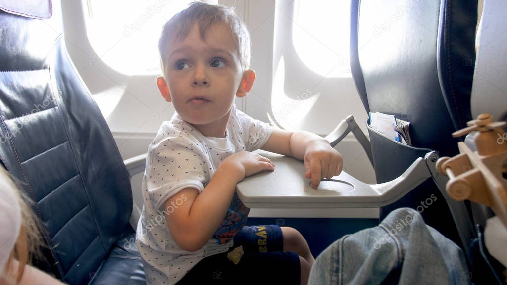 Little boy being scared during flight in airplane looking at mother