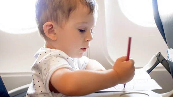 Портрет крупным планом милого мальчика, рисующего картинку с красочными карандашами в самолете — стоковое фото
