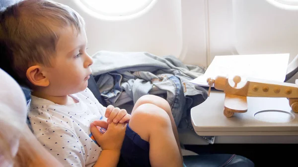 Портрет маленького мальчика, смотрящего на деревянный игрушечный самолет во время полета в самолете — стоковое фото