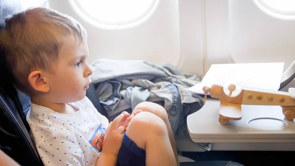 Primer plano tonificado foto de niño lindo sentado en el avión y mirando en pequeño biplano de juguete — Foto de Stock