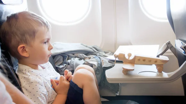 Retrato del niño pequeño sentado en el asiento del pasajero con un avión de juguete de madera — Foto de Stock